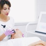 Contact Aesthetician providing a laser facial treatment to a patient in a spa clinic setting.